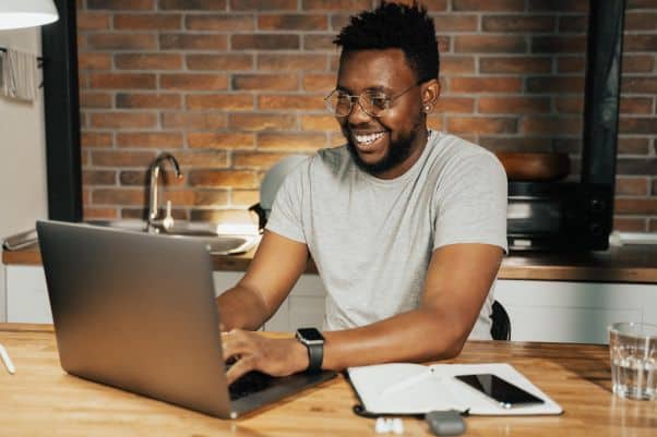 Man in kitchen studies an online Swahili course and smiles.