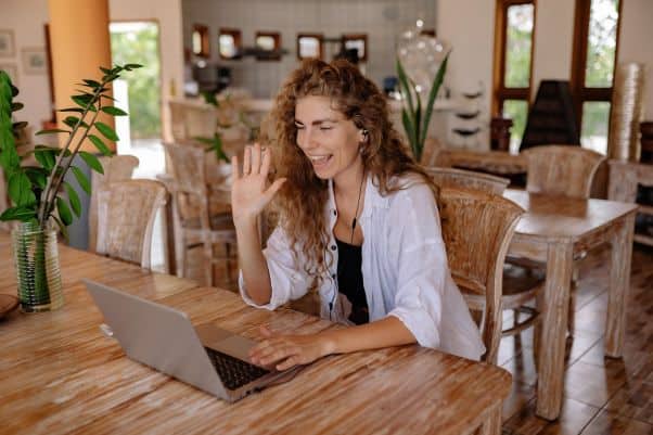 A smiling woman smiles and waves during an online language class 