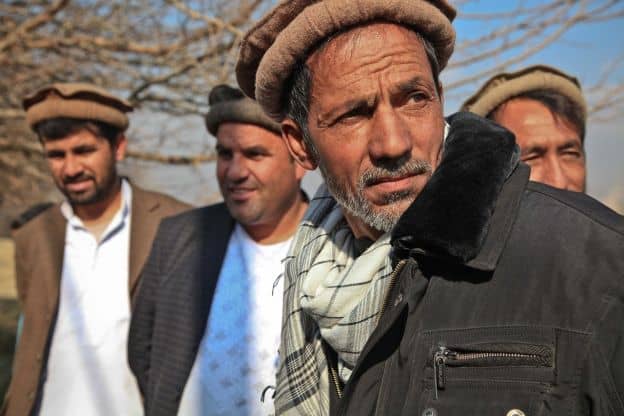 A small group of Afghan men stand in the autumn sun, each wearing a traditional wool cap known as the pakol.