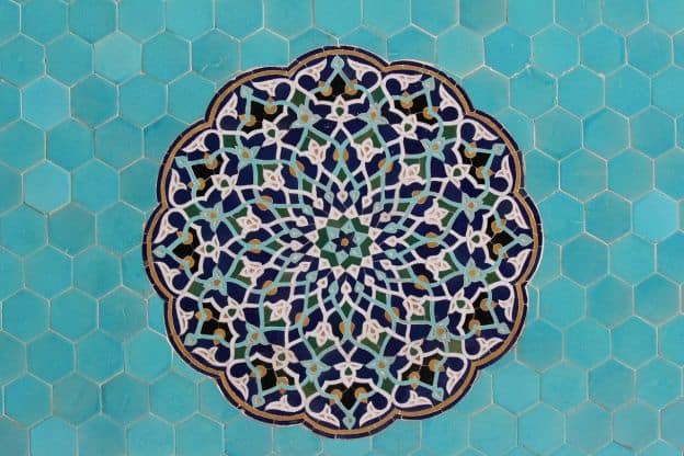 A mosaic of an intricate geometric pattern on a background of light blue tiles; part of the design of a mosque in Ishafan, Iran. The pattern is reminiscent of a rose window.