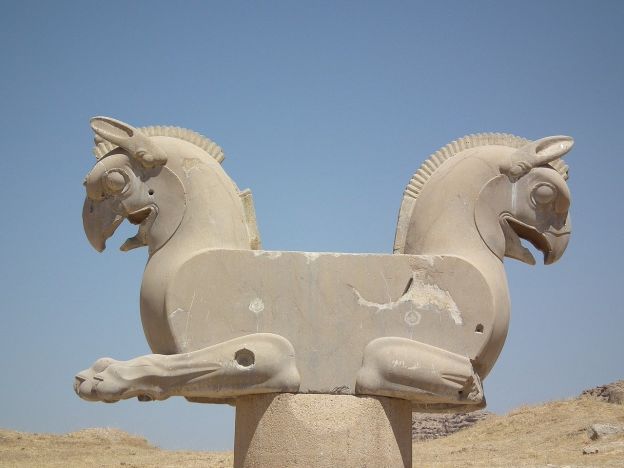 An ancient statue at Persepolis appears to be a double-headed horse, with matching manes and beak-like face, against a desert backdrop.