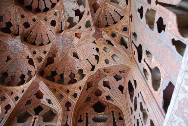 A view upward to the elaborate ceiling of the Music Hall at the Ālī Qāpū Palace at Isfahran, Iran. The intricate designs, with archways in numerous geometric shapes, are painted in detailed designs.