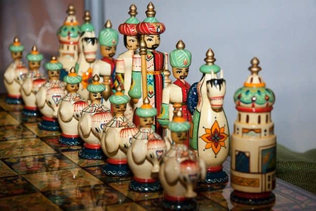 Colorful, carved chess figures in Persian garb stand guard on a reflective chess board.