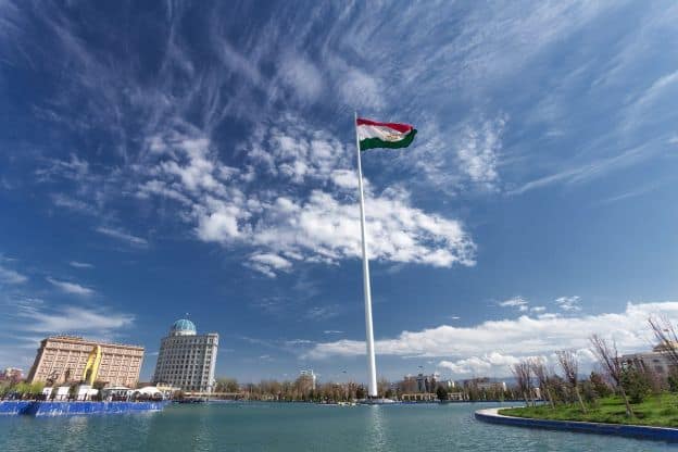 Two modern buildings rise up next to the river in Dushanbe, the capital of Tajikistan. A Tajik flag graces the center of the scene.