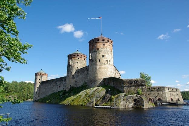 St. Olaf's Castle, with its round turrets and high walls, rises above the water on a clear, sunny day in Savonlinna, Finland. 