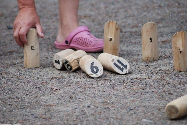 A close-up of a player of a Finnish/Karelian skittles game, this image shows numbered wooden stakes planted in sandy soil