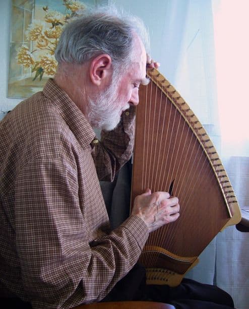A man is seated while playing the kantele, a wooden stringed instrument (similar to a zither) that's traditional in Finland.