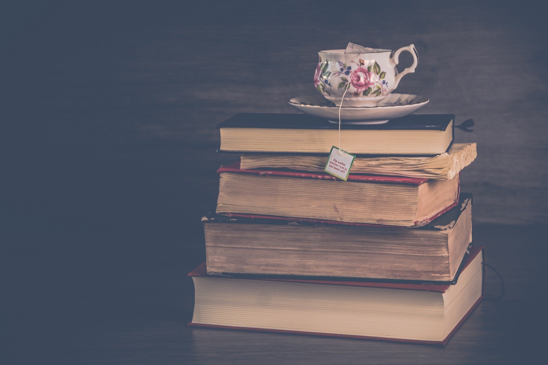A stack of five books with a tea cup resting on top.