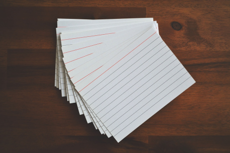 A pile of blank flashcards spread out on a wood desk. 